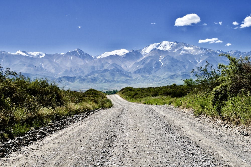 gray dirt road between green grass field and mountains under blue sky during daytime