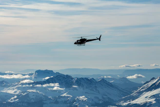 A sleek helicopter flying over the snow-capped peaks of the Himalayas during sunrise.