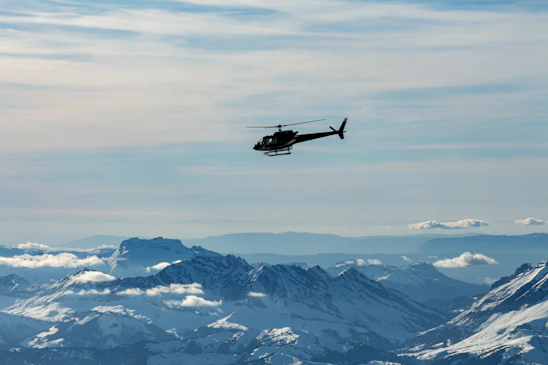 A scenic helicopter flying over the majestic Himalayas with vibrant yellow and blue branding visible.