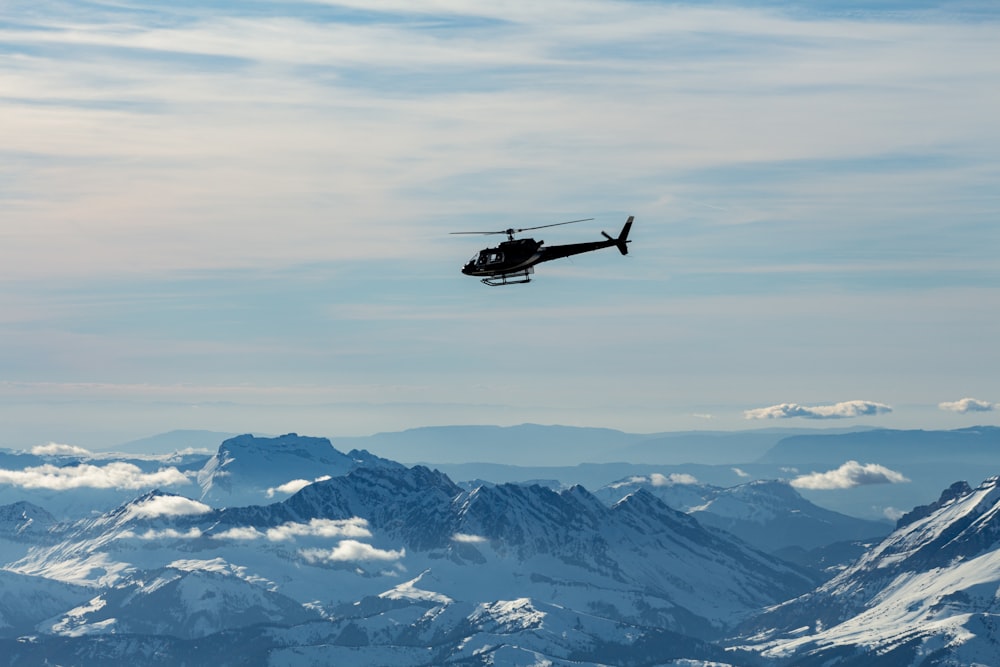 black helicopter flying over snow covered mountains during daytime