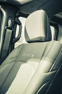 The interior of a vehicle featuring a front passenger seat with the word 'Sahara' embroidered on the fabric. The seatbelt hangs on the side, and part of the doorframe and window is visible. The image is captured in a muted, somewhat vintage style.