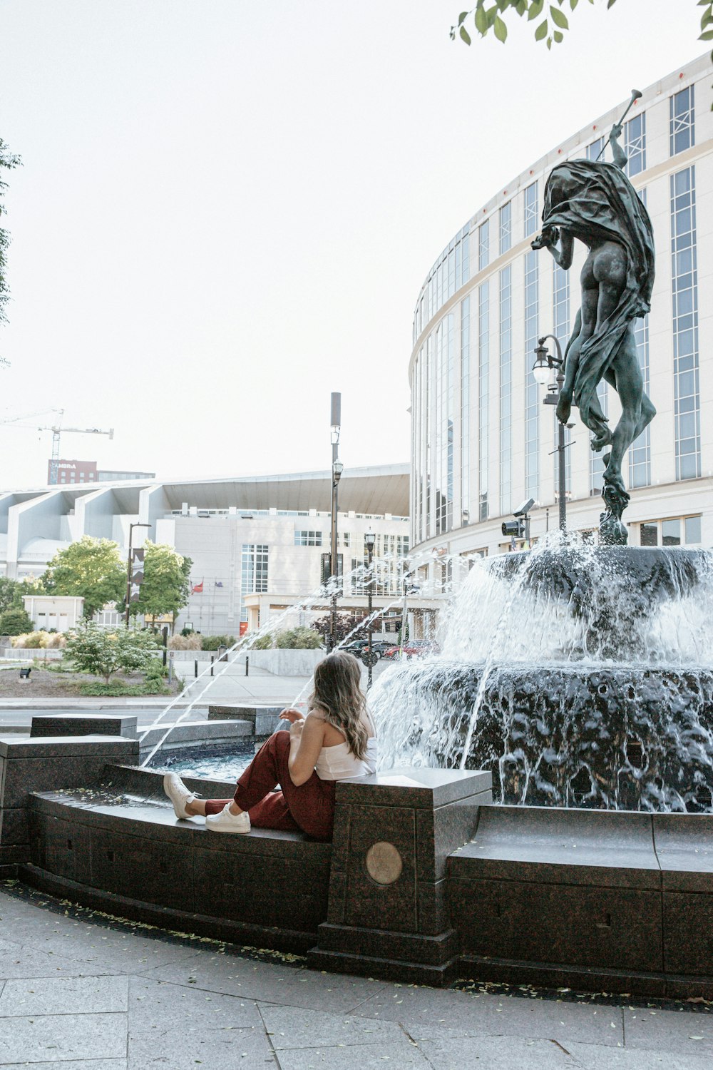 woman in pink shirt sitting on brown wooden bench near fountain during daytime