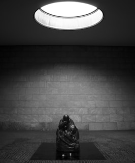 A photograph of a dimly lit sculpture casting long shadows that evoke solitude and reflection.