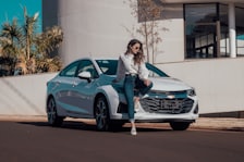 woman in white long sleeve shirt and blue denim jeans sitting on blue bmw coupe
