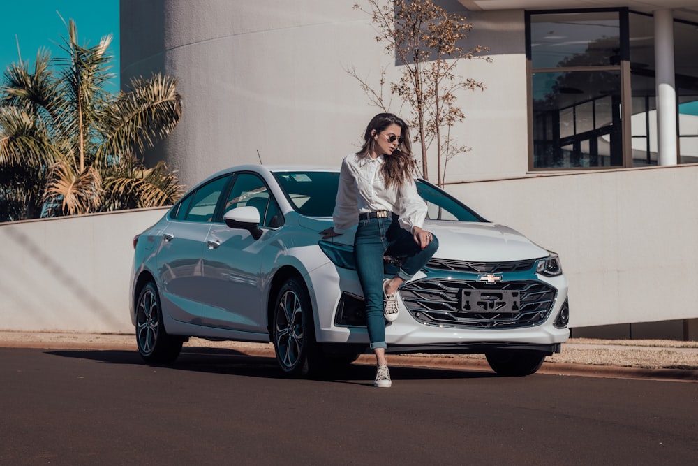 woman in white long sleeve shirt and blue denim jeans sitting on blue bmw coupe