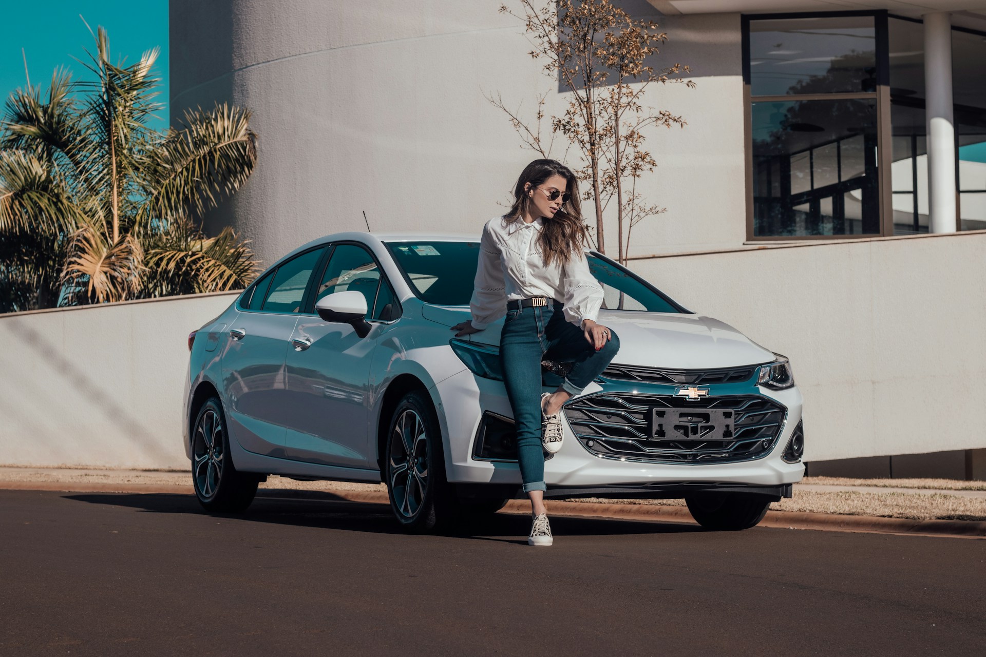 woman in white long sleeve shirt and blue denim jeans sitting on blue bmw coupe