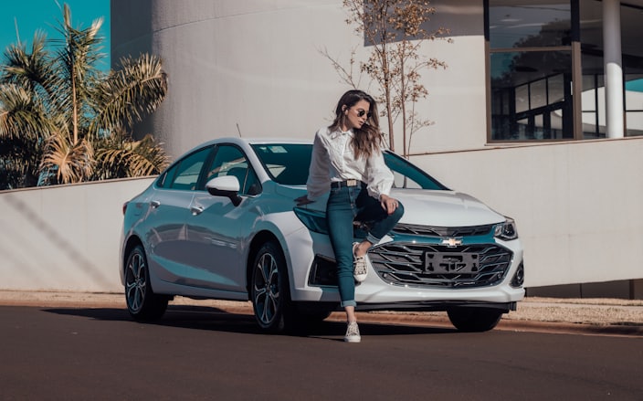 woman in white long sleeve shirt and blue denim jeans sitting on blue bmw coupe