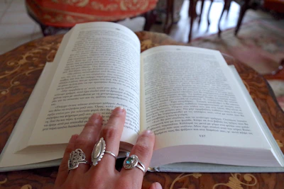 Close-up of hands exchanging a well-loved book, surrounded by charcoal-toned cushions and soft sand walls.