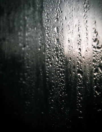 A close-up of raindrops sliding down a foggy window pane.