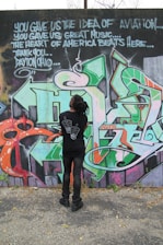 woman in black long sleeve shirt and black pants standing beside graffiti wall during daytime