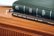 A close-up of two books stacked on a wooden surface. The top book is a green Holy Bible with the title and Christian Standard Bible label in white text. Below it, a dark brown book titled 'Evil And The Justice Of God' is visible.