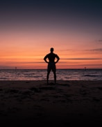 silhouette of man and woman standing on beach during sunset