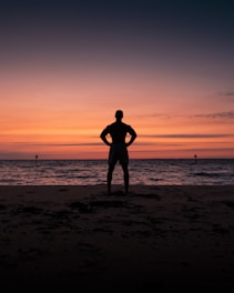 silhouette of man and woman standing on beach during sunset