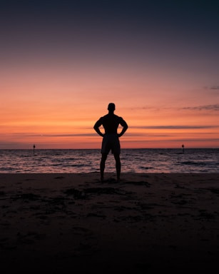 silhouette of man and woman standing on beach during sunset
