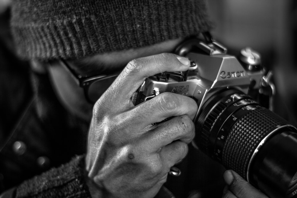 grayscale photo of person holding black and silver nikon dslr camera