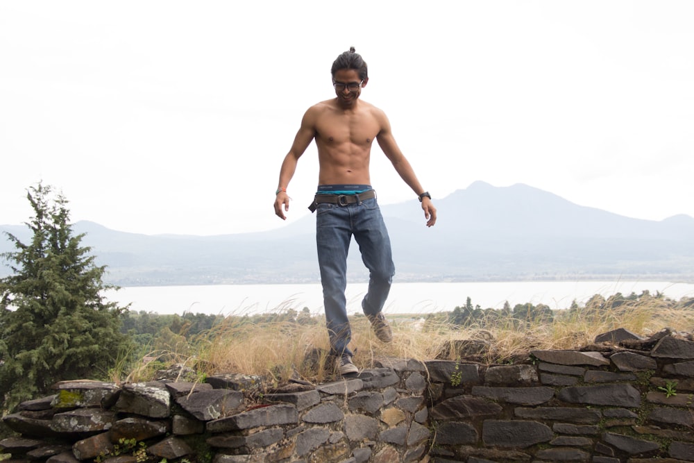 topless man in blue denim jeans standing on rock during daytime