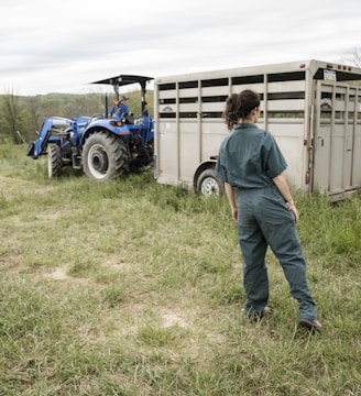 man in blue denim jeans standing beside blue tractor during daytime
