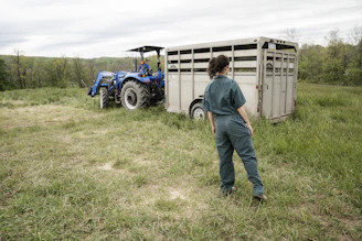 man in blue denim jeans standing beside blue tractor during daytime