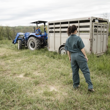 man in blue denim jeans standing beside blue tractor during daytime