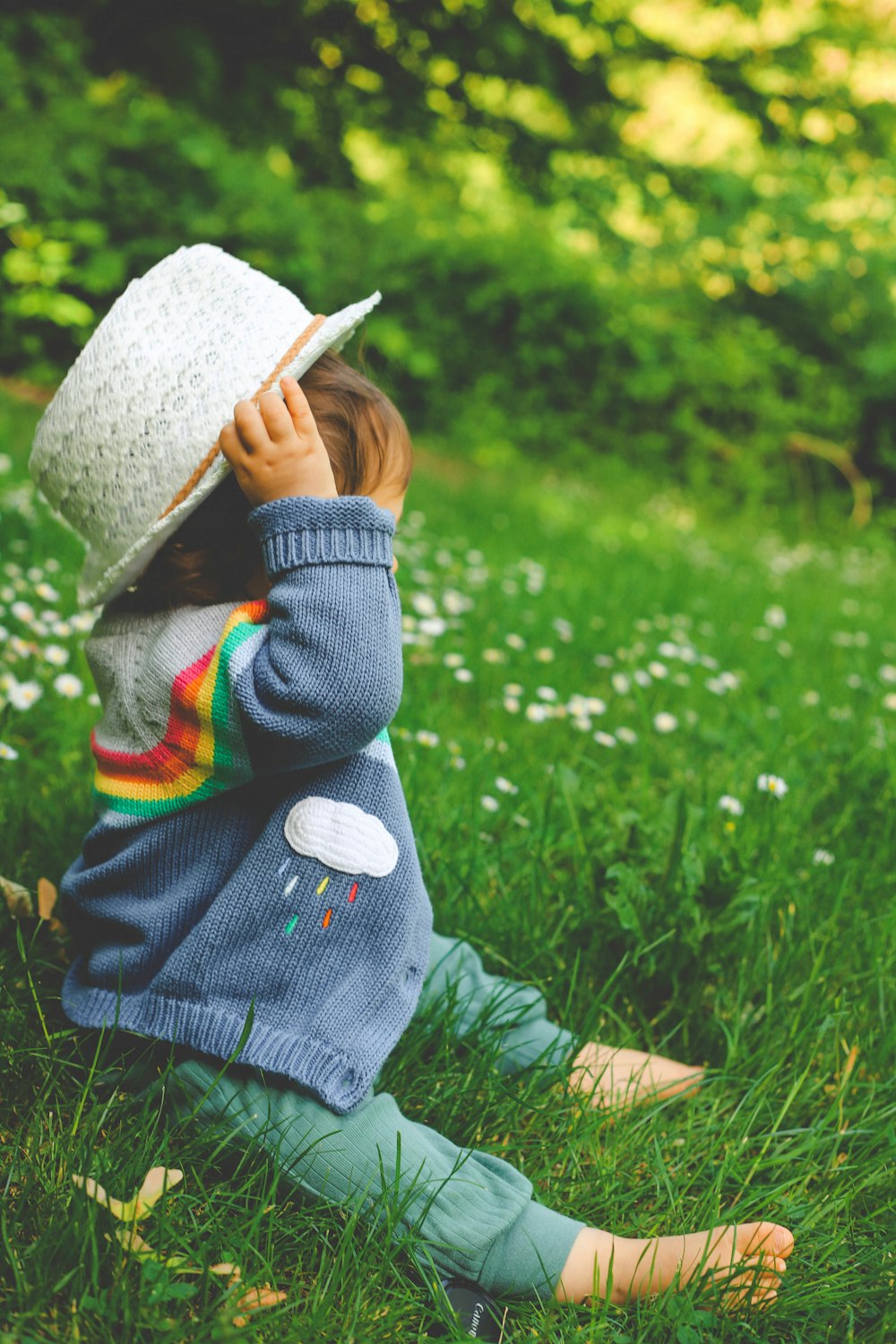 Enfant en veste grise et chapeau blanc debout sur le champ d’herbe verte pendant la journée