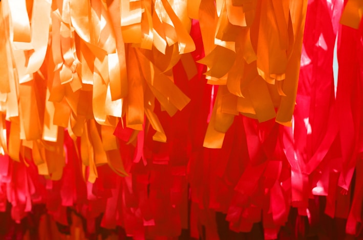 A vibrant display of golden ribbons intertwined with deep red fabric, reflecting the brand's signature colors.