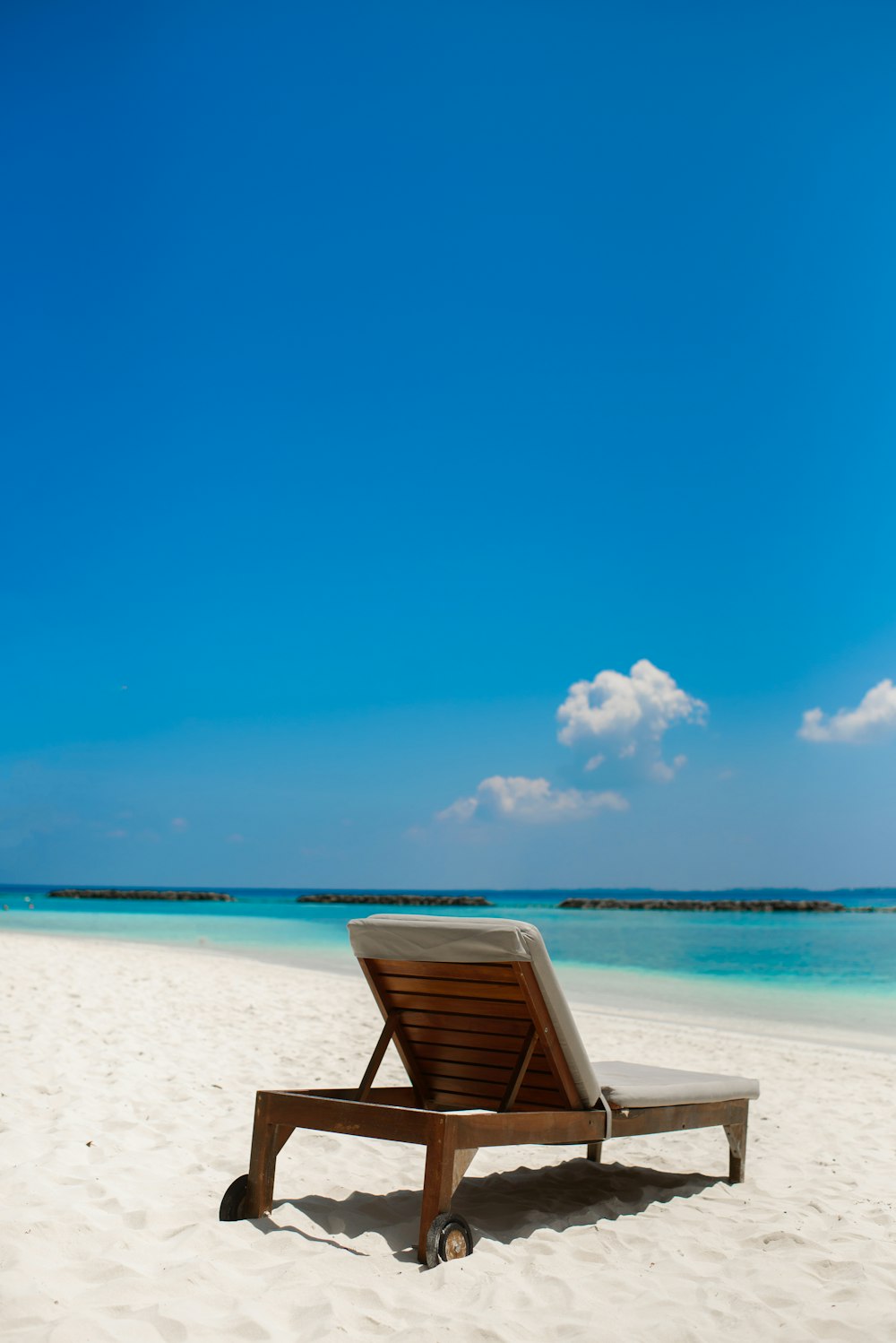 cadeira dobrável de madeira marrom na praia de areia branca durante o dia
