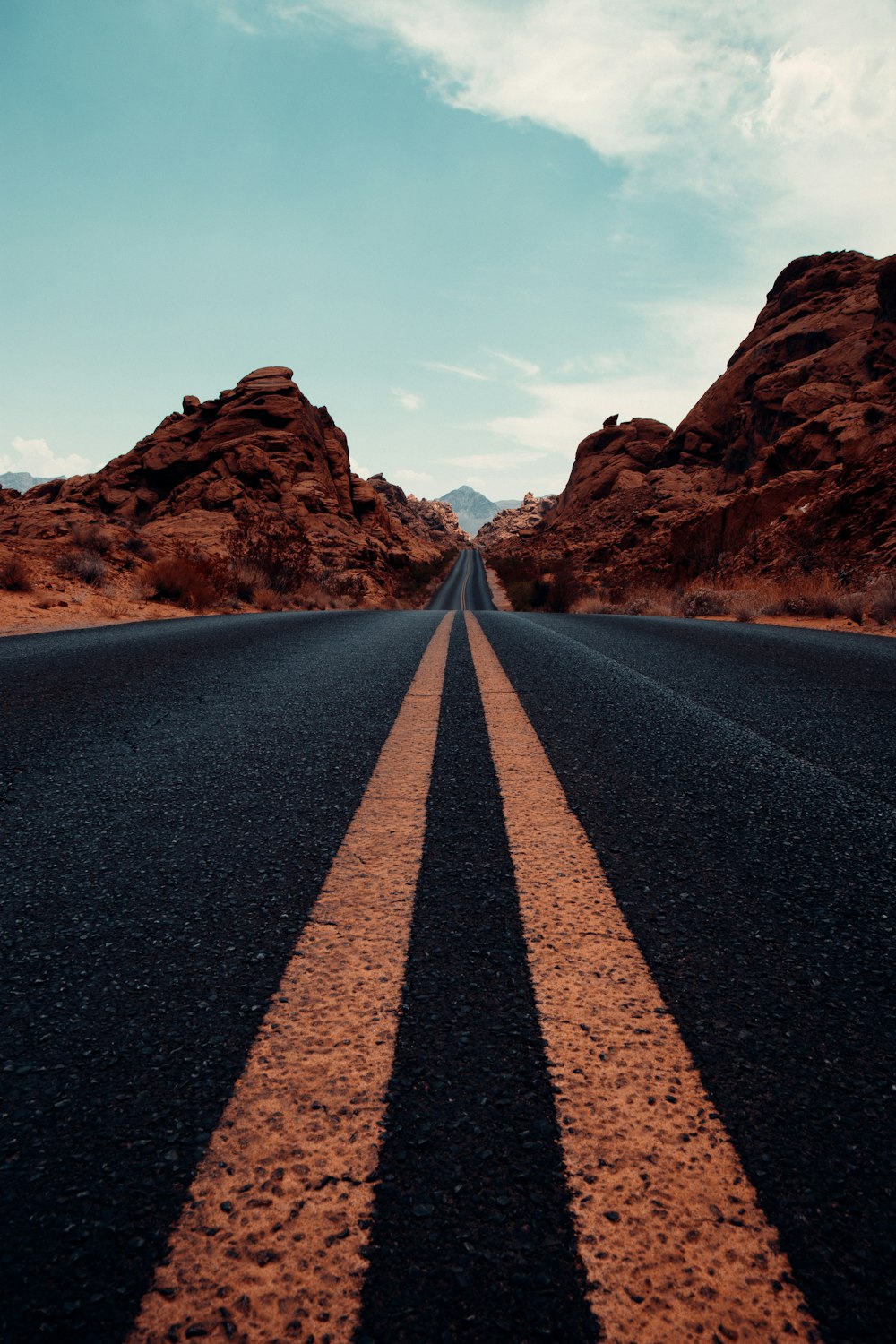 Carretera de asfalto negro entre montañas marrones bajo cielo azul durante el día