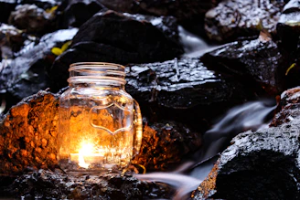 A softly glowing luxury candle nestled among smooth stones and dried botanicals, casting a warm, tranquil light.