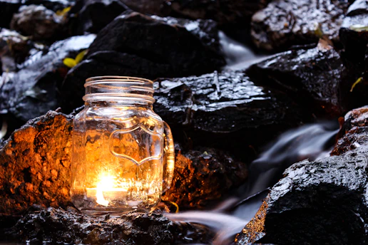 A softly glowing luxury candle nestled among smooth stones and dried botanicals, casting a warm, tranquil light.