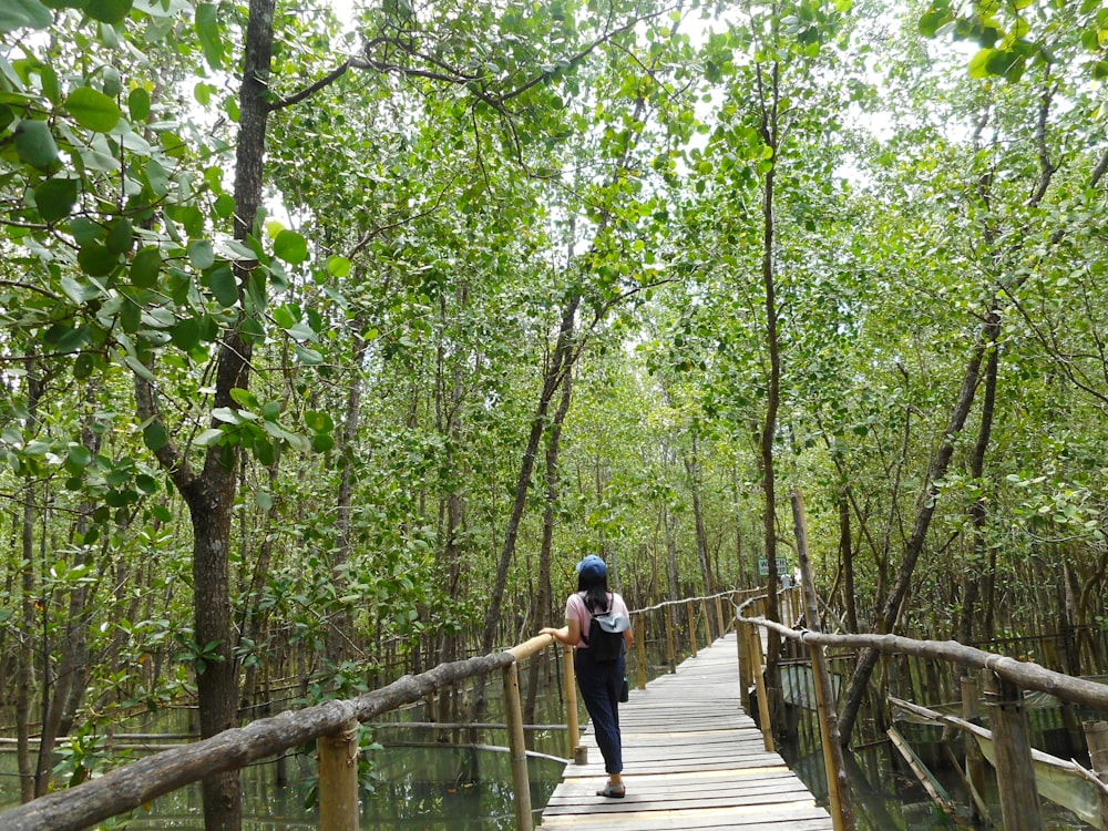 man in blue jacket and black pants walking on wooden bridge in forest during daytime