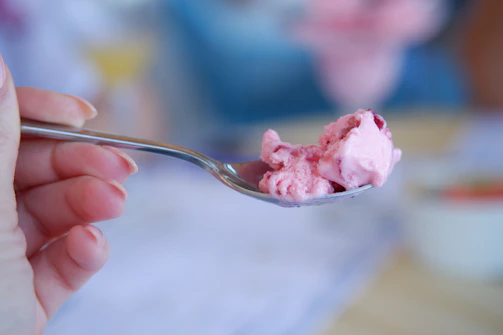 Close-up of a hand holding a creamy vanilla ice cream scoop with a soft pink background.