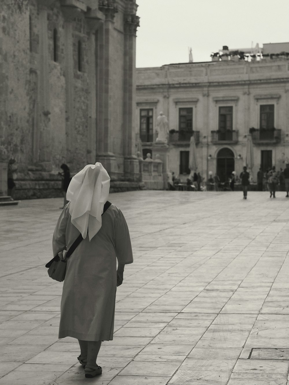 grayscale photo of woman in white hijab standing on sidewalk