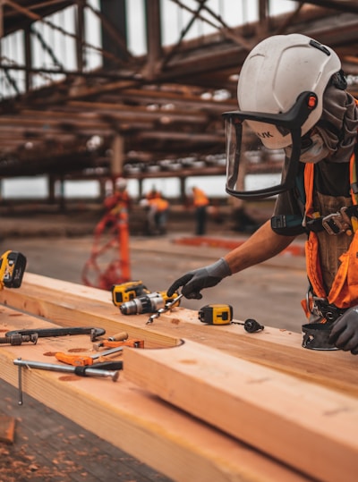 man in orange and black vest wearing white helmet holding yellow and black power tool