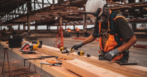 man in orange and black vest wearing white helmet holding yellow and black power tool