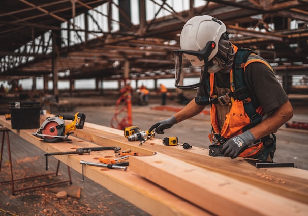 man in orange and black vest wearing white helmet holding yellow and black power tool