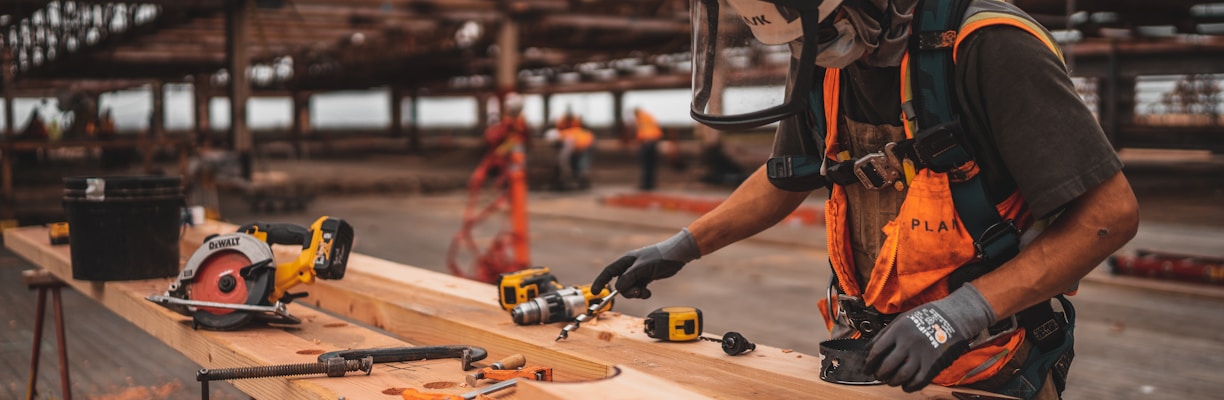 man in orange and black vest wearing white helmet holding yellow and black power tool