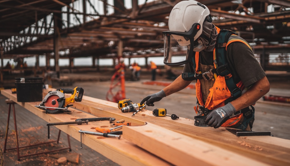 man in orange and black vest wearing white helmet holding yellow and black power tool