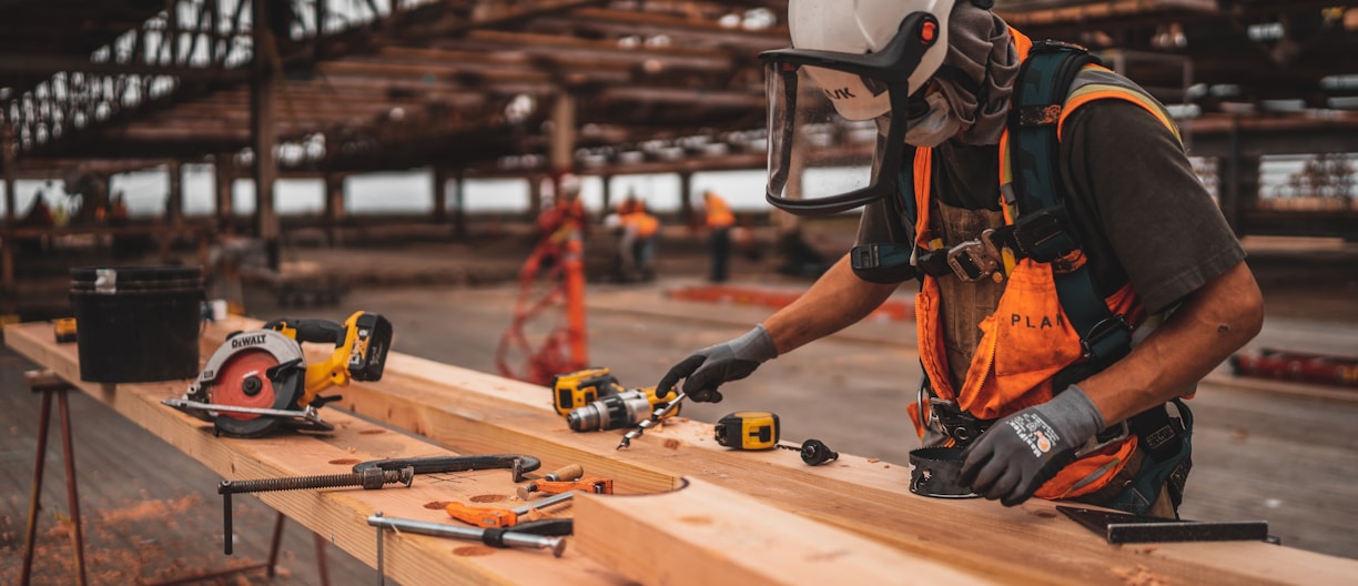 man in orange and black vest wearing white helmet holding yellow and black power tool