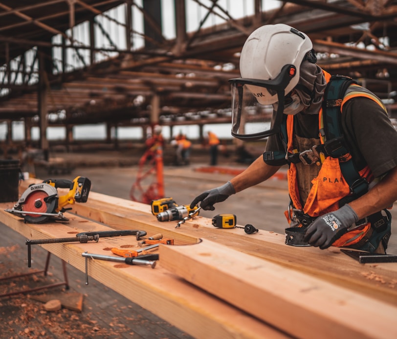 man in orange and black vest wearing white helmet holding yellow and black power tool