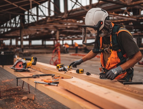 man in orange and black vest wearing white helmet holding yellow and black power tool