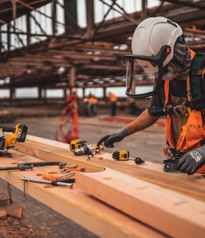 man in orange and black vest wearing white helmet holding yellow and black power tool