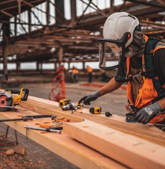 man in orange and black vest wearing white helmet holding yellow and black power tool