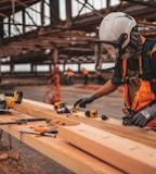 man in orange and black vest wearing white helmet holding yellow and black power tool