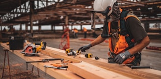 man in orange and black vest wearing white helmet holding yellow and black power tool