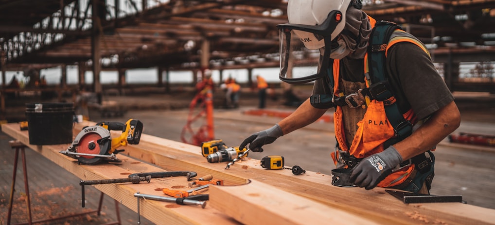 man in orange and black vest wearing white helmet holding yellow and black power tool