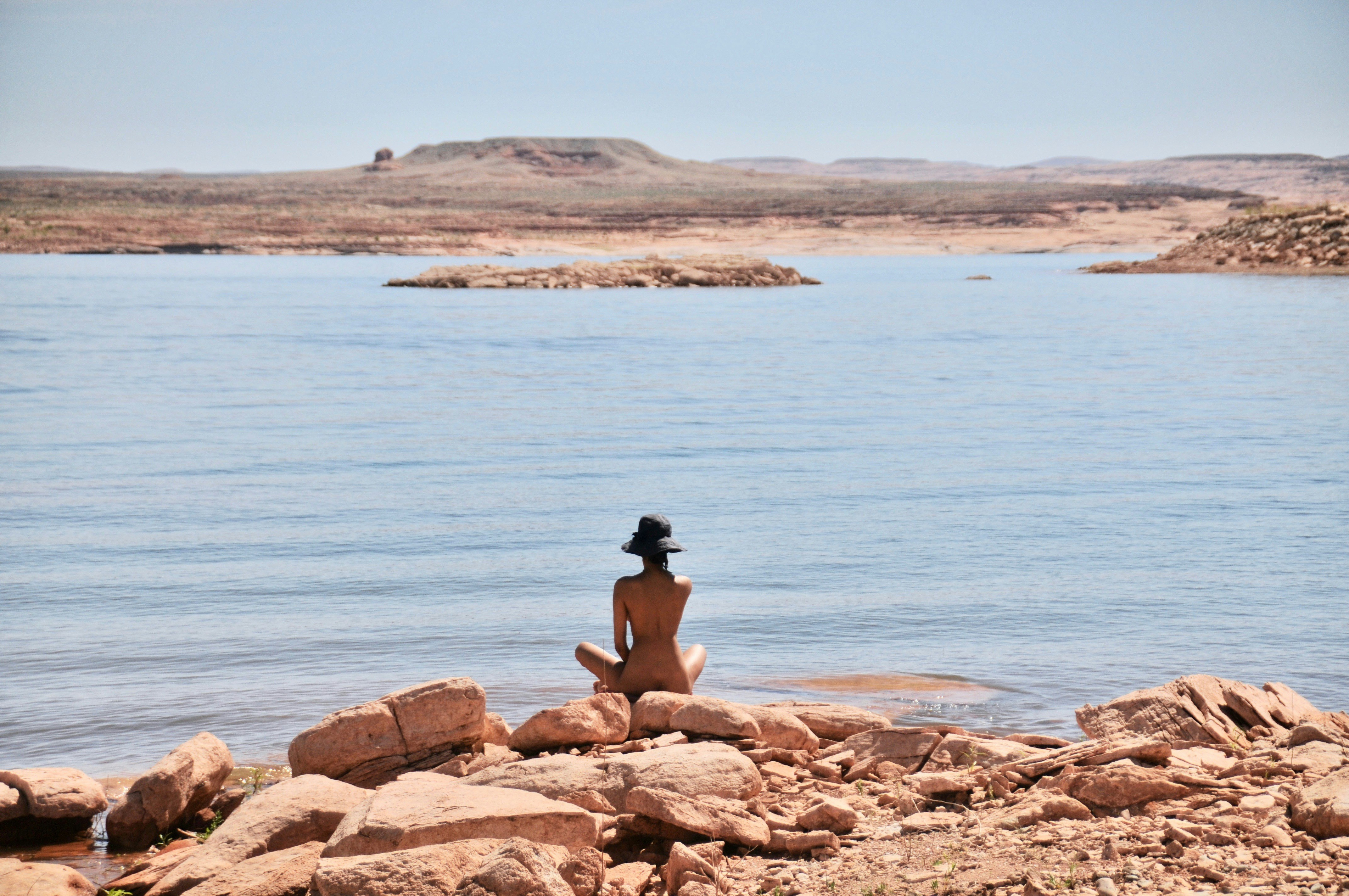 woman in black tank top sitting on brown rock near body of water during daytime