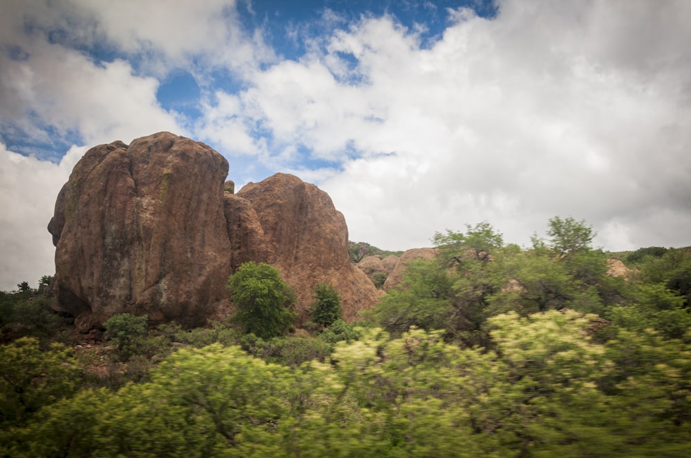 green trees near brown rock formation under blue sky and white clouds during daytime