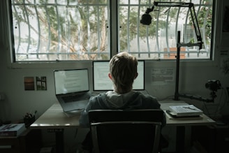 woman in gray hoodie sitting on chair in front of laptop computer