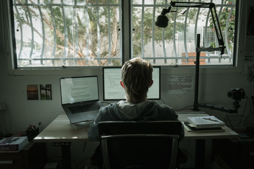 woman in gray hoodie sitting on chair in front of laptop computer