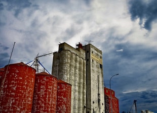 A bustling grain storage facility with workers inspecting large silos under a bright sky.